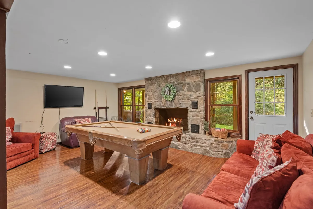 A spacious entertainment den with a pool table, cozy sofa seating, a large stone fireplace, and a TV. The relaxed mood is ideal for group games, movie nights, or simply enjoying each other’s company by the fire.