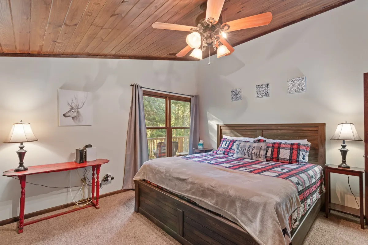 A bright bedroom with colorful bedding, a wooden ceiling, large window letting in natural light, and decorative wall art. The room feels tranquil and welcoming, ideal for unwinding after a day of activity.