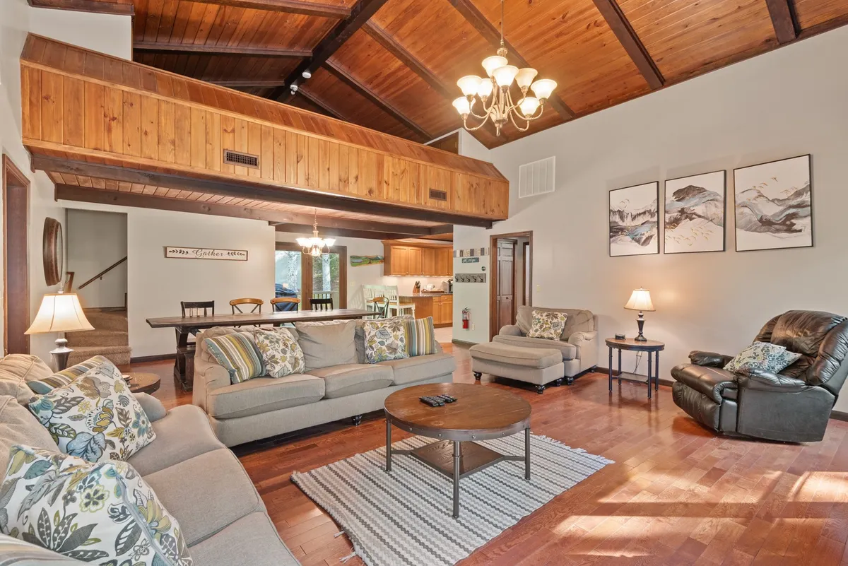 A cozy, warm living room with a sofa set adorned with colorful cushions, a coffee table for snacks or board games, tasteful wall art, and a stylish chandelier overhead. The space is designed for relaxing, socializing, and entertaining guests, perfect for movie nights or family gatherings.