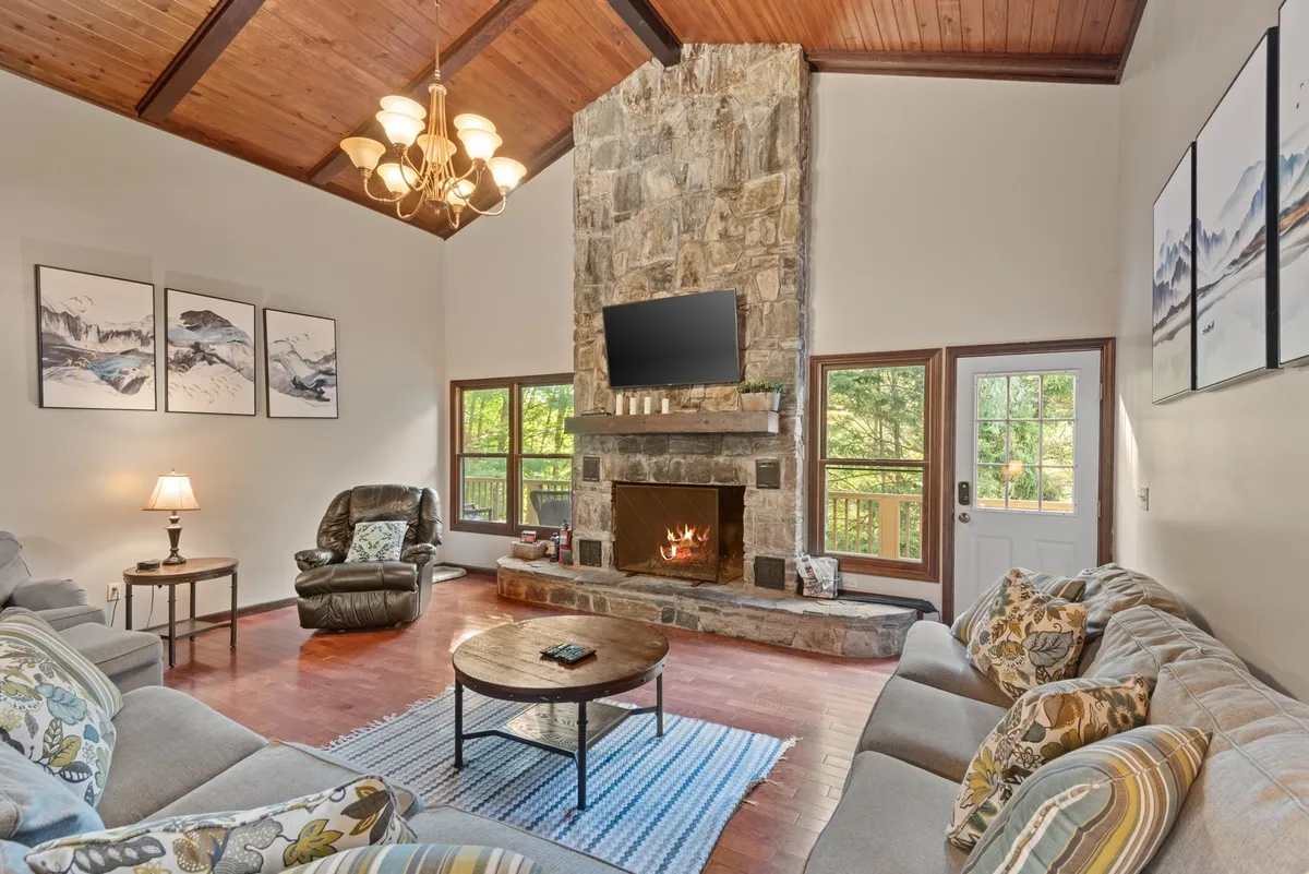 A spacious living area featuring a large stone fireplace, comfortable seating, and a warm wooden ceiling. The setup suggests a welcoming atmosphere ideal for gathering after outdoor activities. The arrangement encourages guests to unwind together, perhaps with a hot drink after a day on the slopes.