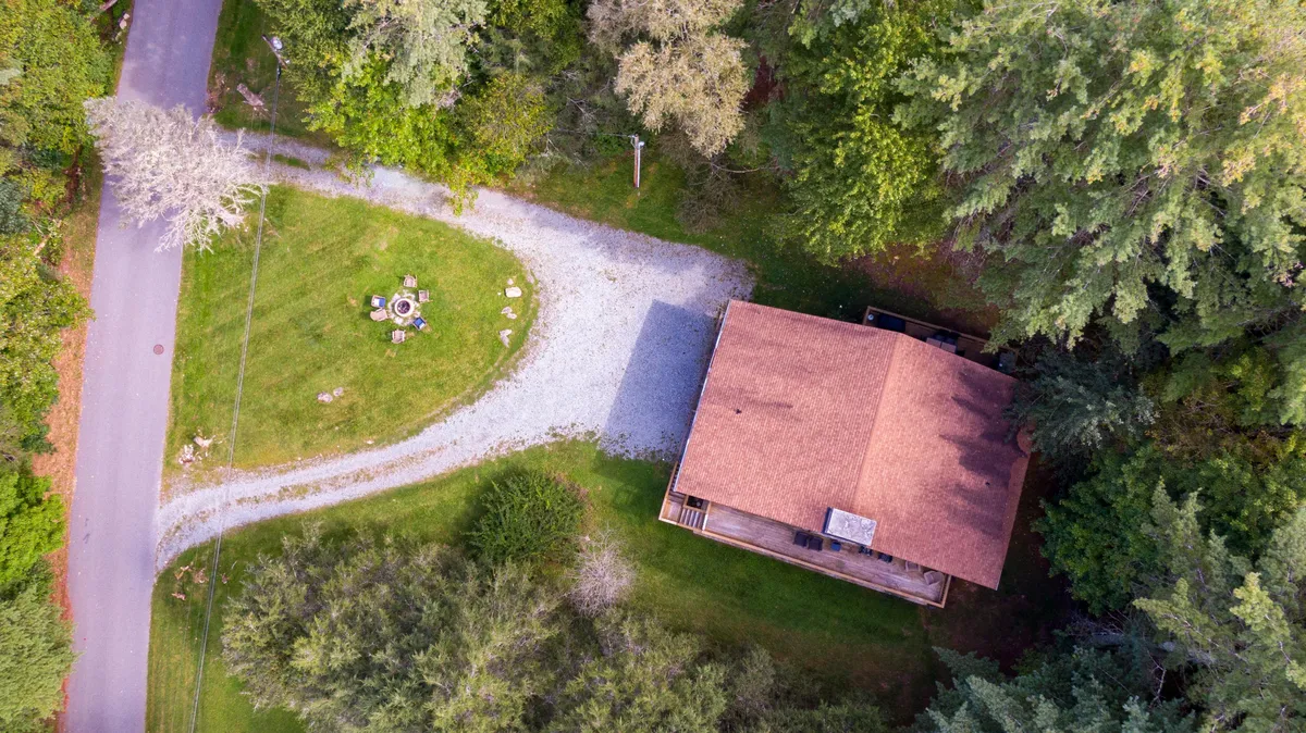 The exterior shot shows the house, a welcoming gravel driveway, a cozy fire pit area, and mature trees all around. The scene feels peaceful and inviting, suggesting a great home base for returning after exploring downtown events, shopping, or dining.