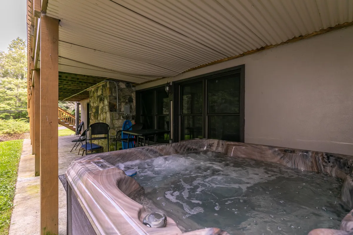 A welcoming outdoor scene featuring a bubbling hot tub with seating beside a stone wall, all nestled into a wooded setting. The area channels relaxation with a touch of luxury, ideal for evening soaks or socializing under the stars.