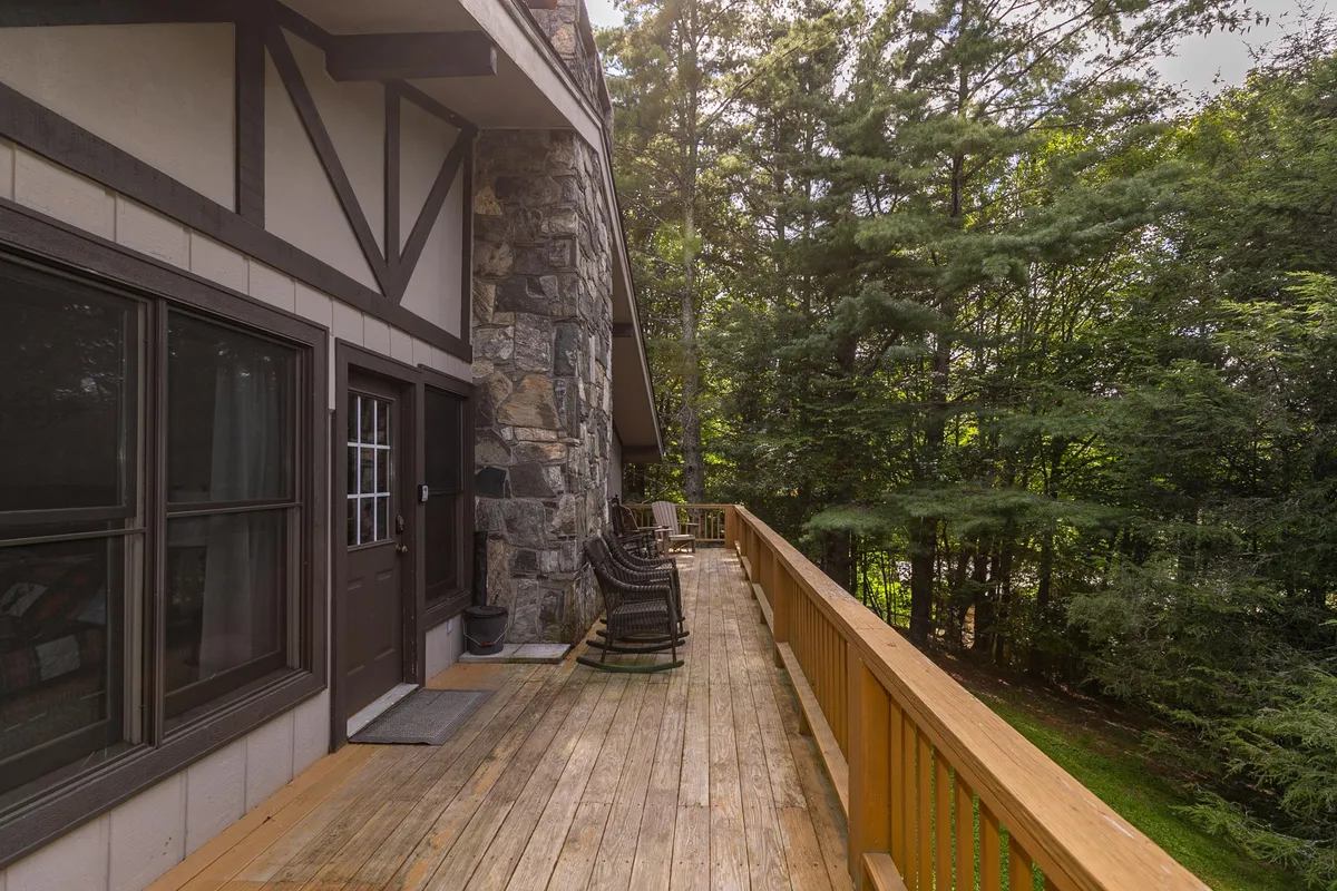 A tranquil wooden deck set against a stone wall, featuring classic wooden rocking chairs and surrounded by lush trees. The area exudes a peaceful, rustic ambiance, perfect for relaxing and enjoying nature.