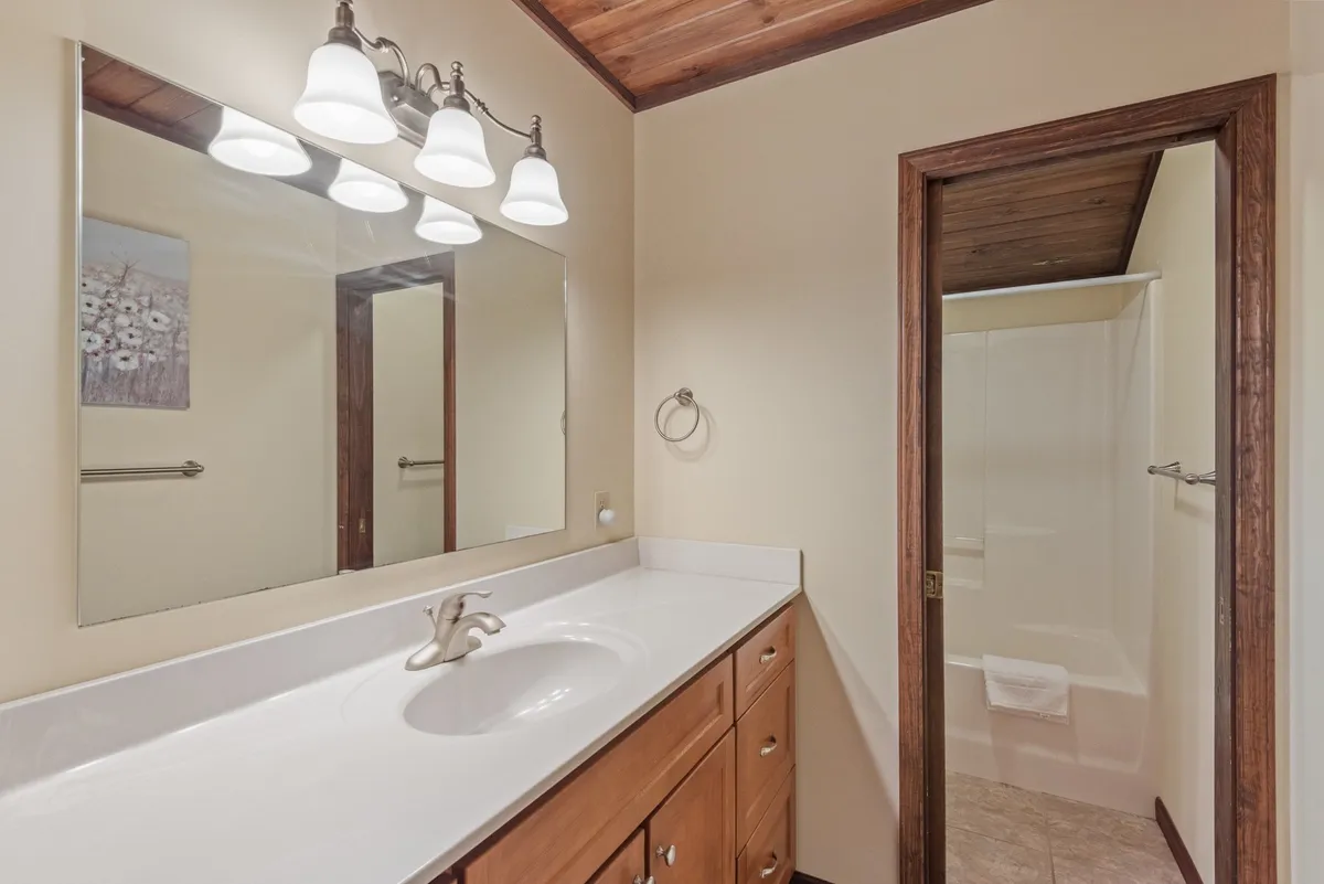 A serene bathroom scene with a vanity, sink, mirror, light fixtures, and a doorway that leads to a shower. The space is bright, clean, and spa-like, supporting routines of relaxation and self-care.