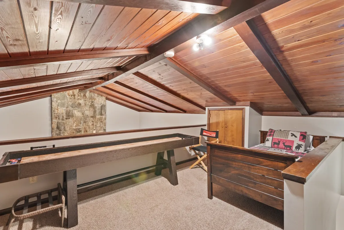 This image features a welcoming, playful interior with a wooden ceiling, a game table perfect for board games or card nights, a bed with a decorative throw pillow, and a stone wall art accent. The scene is set for both play and relaxation, capturing the spirit of in-home entertainment and memorable game nights.