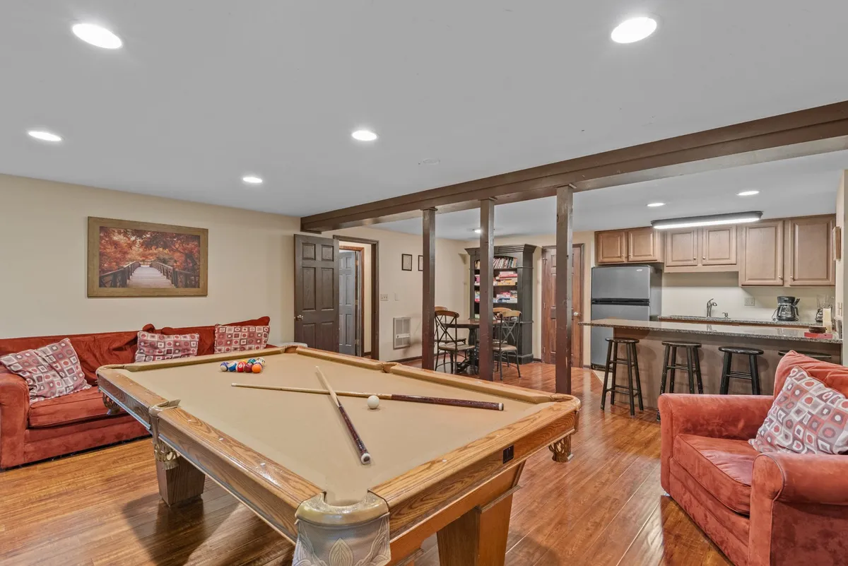A cheerful downstairs recreation area where a pool table, vibrant red couches, and an open kitchen with bar seating invite guests to play, socialize, or grab a snack. The informal atmosphere encourages both competition and togetherness.